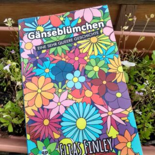 Ein Buch in einem Blumenkasten. Der Titel des Buchs ist "Gänseblümchen - eine sehr queere Geschichte" von Elias Finley.