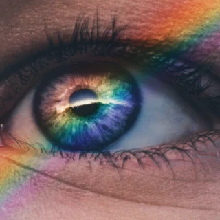 Nahaufnahme eines linken Auges, durch das diagonal ein Regenbogenprisma verläuft.