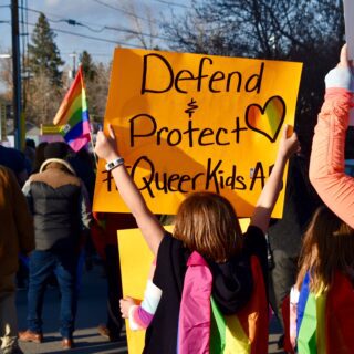 Foto einer Demo, auf dem das Schild zu lesen ist: "Defend and protect queer kids!"
